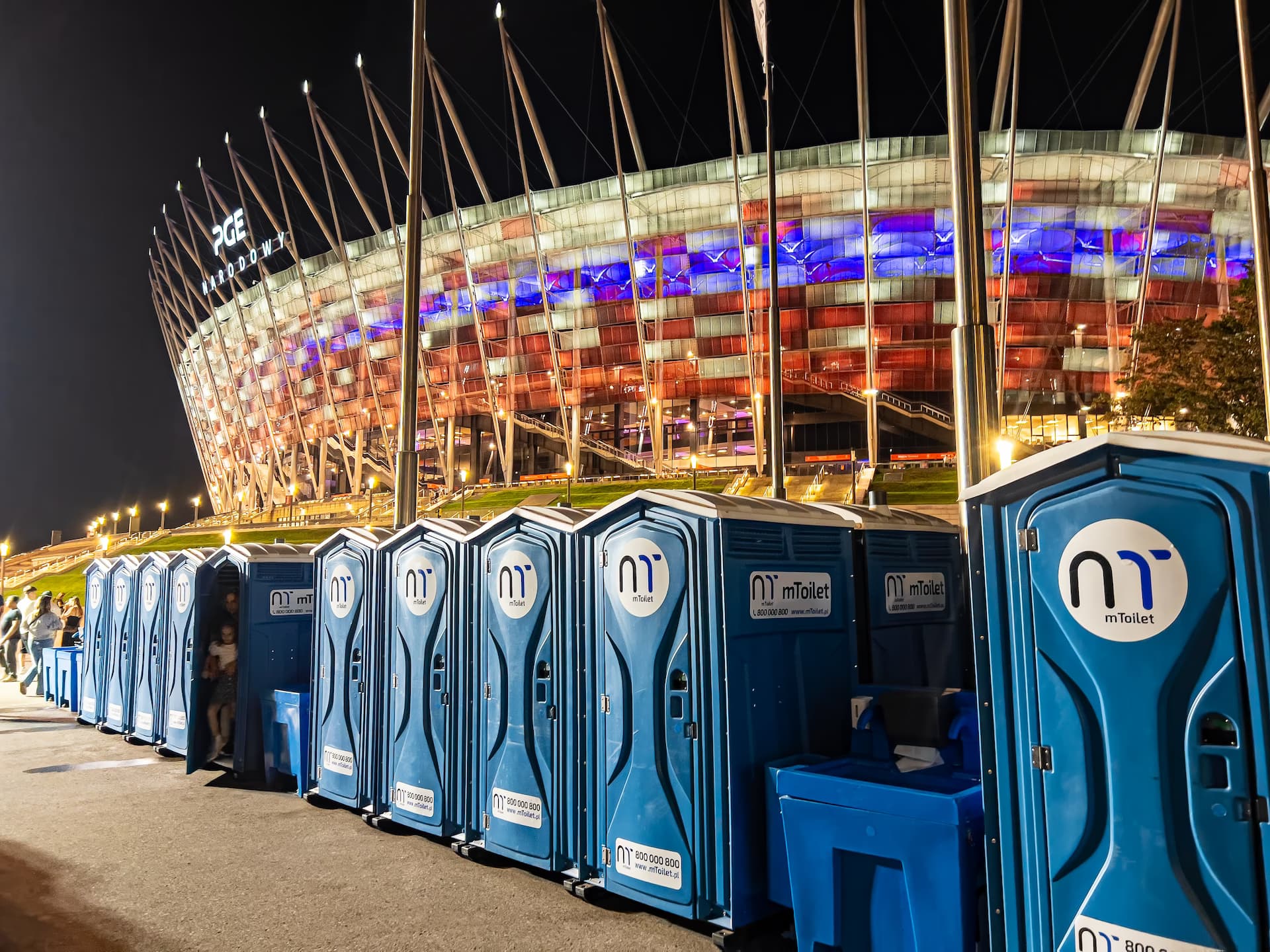 Eine Reihe mobiler mToilet-Toiletten vor einem Stadion bei Nacht